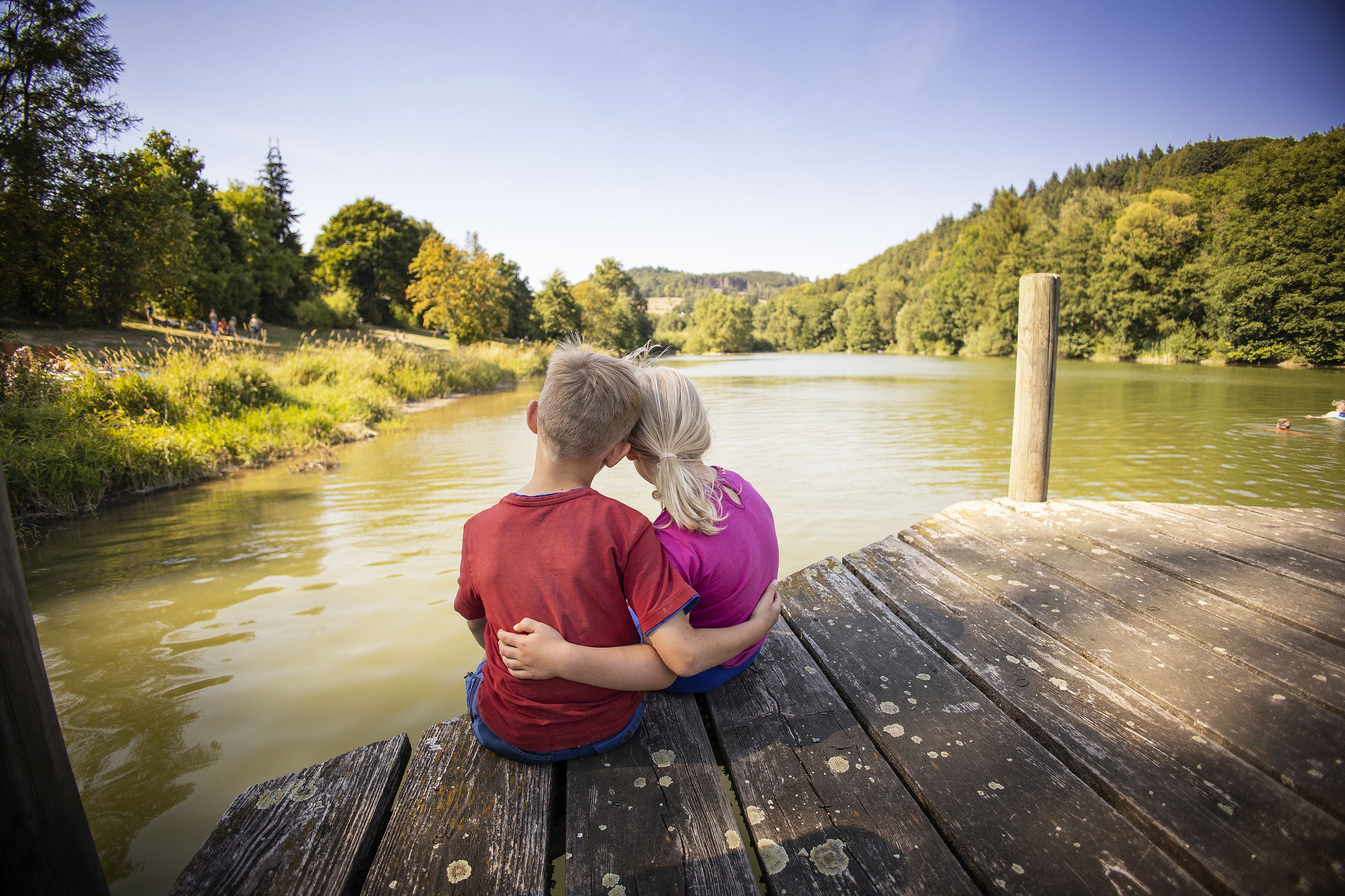 Kinderpaar Arm in Arm auf einem Steg am See