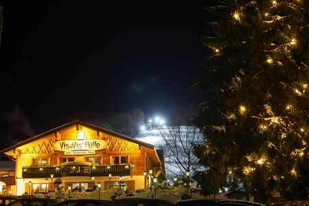 Beleuchtete Vis-à-Vis-Hütte mit Skipiste am Abend 