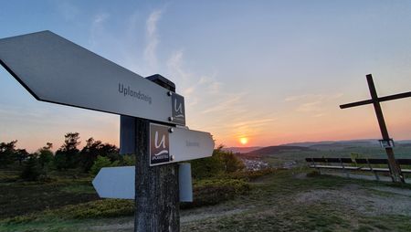 Wegweiser Uplandsteig und Gipfelkreuz bei Sonnenuntergang