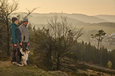 Paar mit Hund vor Bergkulisse im Sonnenuntergang