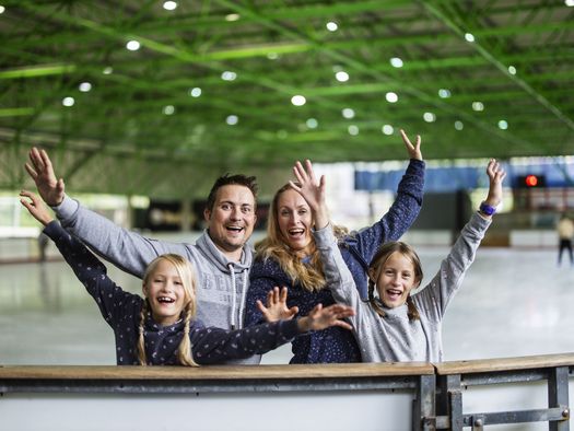 Familie mit erhobenen Armen lacht in die Kamera in der Eissporthalle Willingen