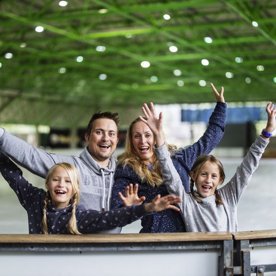 Familie mit erhobenen Armen lacht in die Kamera in der Eissporthalle Willingen