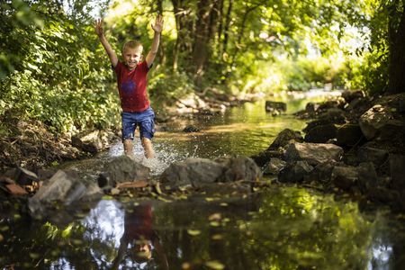 Junge planscht im Wasser eines Bachs