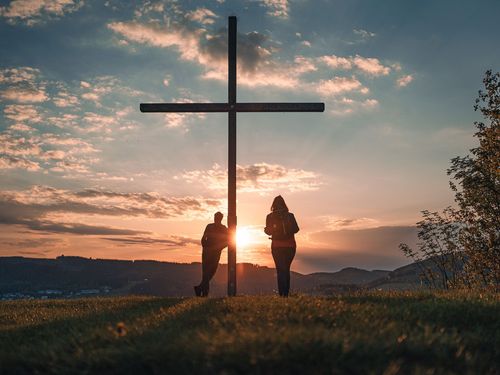 Wanderpaar beim Gipfelkreuz auf dem Orenberg bei Sonnenuntergang