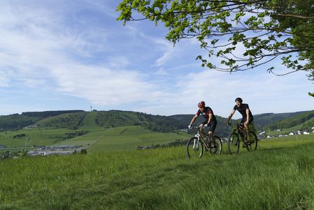 Zwei junge Männer auf Mountainbikes auf einer Wiese, im Hintergrund der Ettelsberg in Willingen